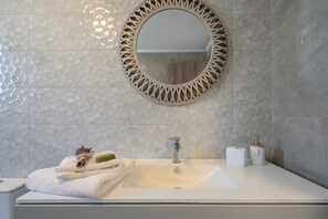 Un baño con un lavabo blanco, un espejo redondo y un perchero con toallas dobladas.