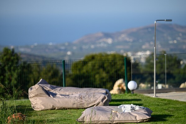 A grassy area with two beige bags and a white object, a street lamp, and a fence with a view of distant mountains.