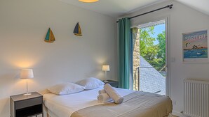 A bedroom with a bed, two bedside tables, a window with curtains, a radiator, and a poster on the wall. - Les Dryades - Villa familiale proche plage (Sarzeau)
