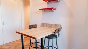 Ein Essbereich mit einem Holztisch, zwei Stühlen, einer weißen Tür und einem an der Wand befestigten Regal.
