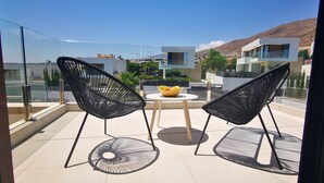 Een balkon met twee zwarte stoelen, een klein rond tafeltje en een schaal fruit.