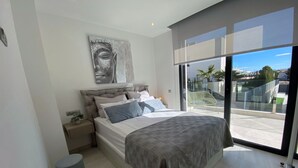 Een moderne slaapkamer met een groot bed, een hoofdbord, een nachtkastje, een klein krukje en een groot raam met uitzicht.
