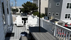 Eine Holzterrasse mit Picknicktischen und -stühlen, einem Grill und einem weißen Zaun.
