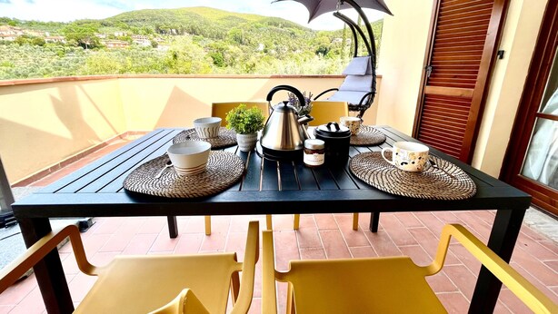 A balcony with a table set for two, featuring a view of a hilly landscape. - Family room (Toscana)