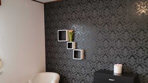 Een slaapkamer met een bed, een stoel, een dressoir en een wandplank met een vaas.