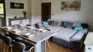 Een moderne woonkamer met een eethoek, een grijze bank met gestreepte kussens en een hanglamp.