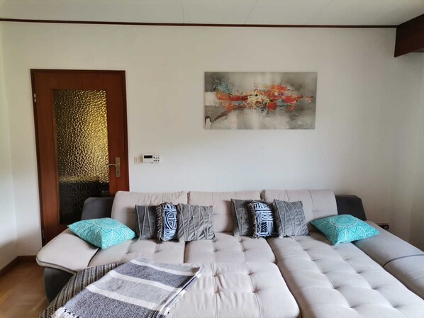 Ein modernes Wohnzimmer mit einem großen beigen Sofa, Kissen mit Muster und einem modernen abstrakten Gemälde an der Wand.