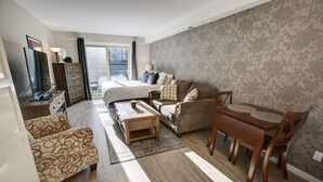 A modern hotel room with a bed, sofa, coffee table, and dining table. - Creekside Mountain View Studio!Patio + BBQ,Pool,Parking & Walk to Shops and Lakes! (Whistler)