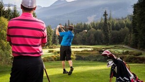 A golf course with a player in a blue shirt and a spectator in a pink striped shirt. - Creekside Mountain View Studio!Patio + BBQ,Pool,Parking & Walk to Shops and Lakes! (Whistler)