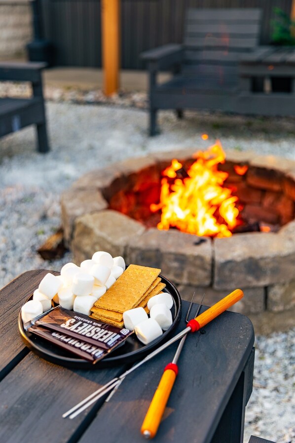 Een kampvuur met een zwarte grill en marshmallows, chocolade en een set voor s'mores op een houten tafel.