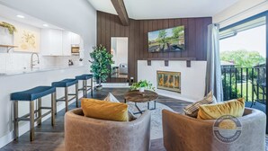 A modern living room with a fireplace, a kitchen with white cabinets, and a balcony with outdoor furniture. - Modern Lake Geneva Condo with Pool and Patio (Lake Geneva)