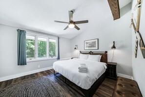 A bedroom with a bed, a ceiling fan, a window with curtains, a bedside table, and a nightstand.