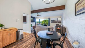 A modern kitchen with a dining area, wooden cabinets, a round table, and a view to a living room. - Modern Lake Geneva Condo with Pool and Patio (Lake Geneva)
