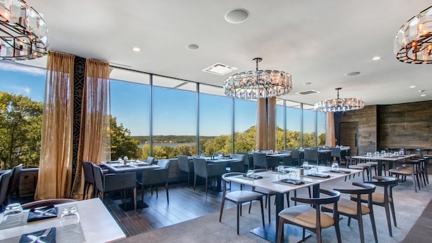 A modern restaurant with large windows offering a scenic view, elegant chandeliers, and neatly arranged tables and chairs. - Modern Lake Geneva Condo with Pool and Patio (Lake Geneva)