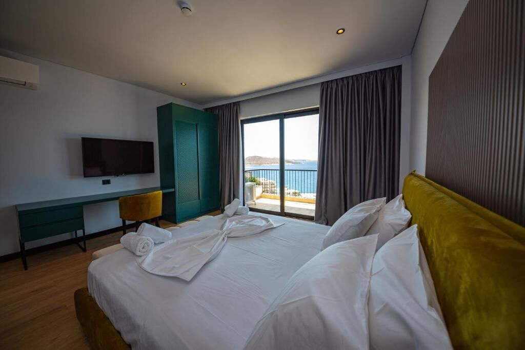 Une chambre d’hôtel avec un lit, un bureau, une télévision et une vue sur la mer.