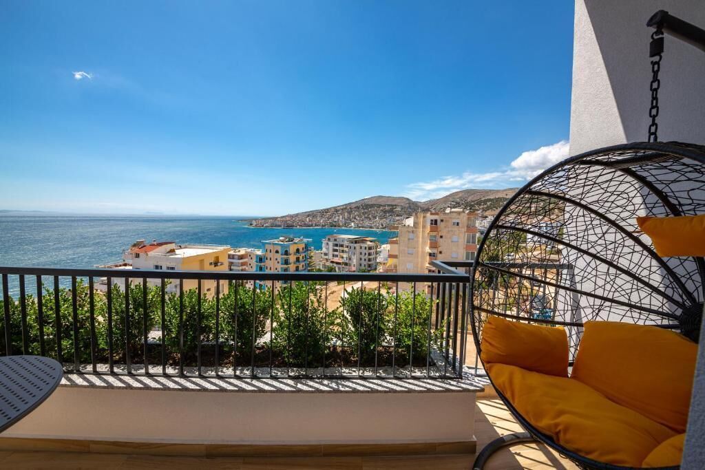 Un balcón con una silla colgante y vistas al mar, con edificios al fondo.