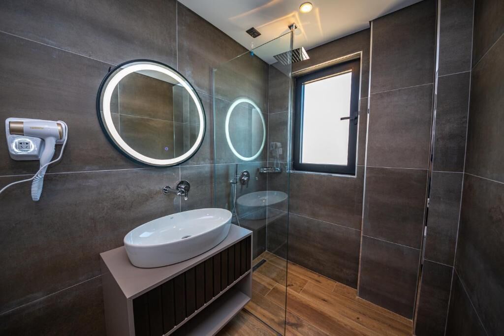 A modern bathroom with a large mirror, a round mirror, a white sink, and a handheld hair dryer.
