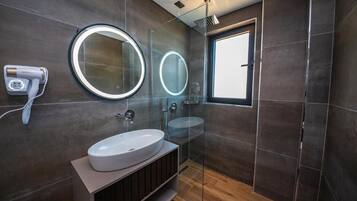 A modern bathroom with a large mirror, a round mirror, a white sink, and a handheld hair dryer.