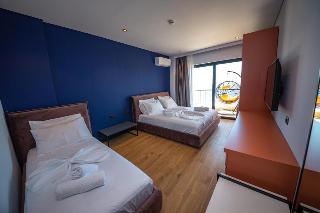 A hotel room with two beds, a TV, and a balcony with a hanging chair.
