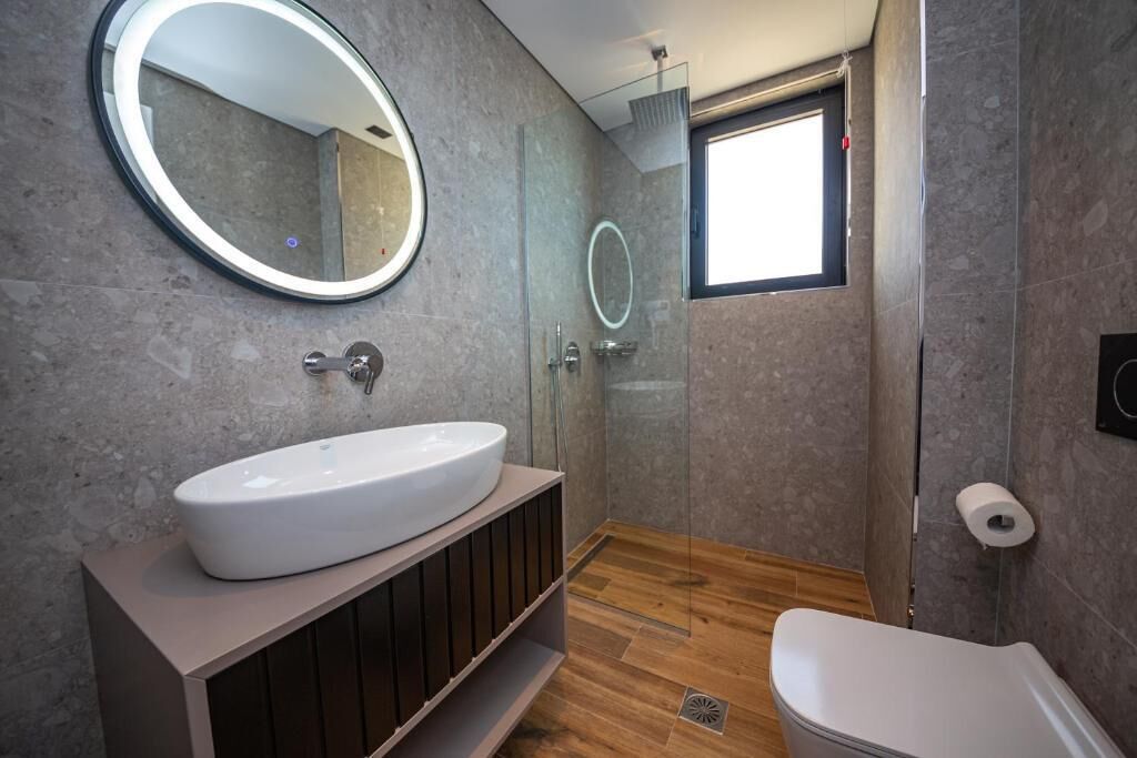 A modern bathroom with a large oval sink, a round mirror, and a glass-enclosed shower.