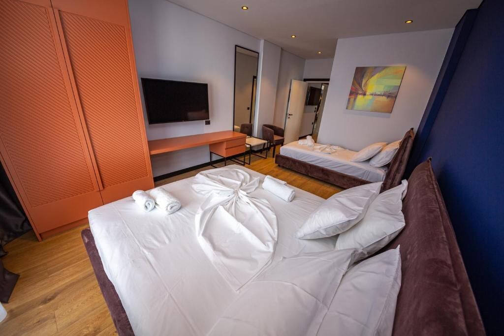 A hotel room with a large bed, a desk, a chair, a TV, and a painting on the wall.