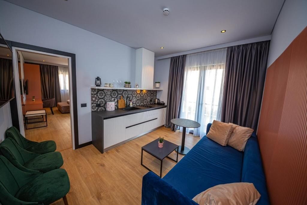 A modern living room with a blue sofa, a small coffee table, and a kitchen area with a patterned backsplash.