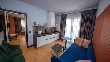 Uma sala de estar moderna com um sofá azul, uma pequena mesa de centro e uma área de cozinha com um revestimento de parede estampado.