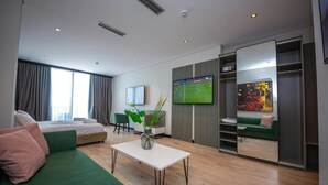 A modern hotel room with a bed, green sofa, a small table with a vase, a TV, and a wardrobe. - Apart-Hotel Lili2 (Sarandë)