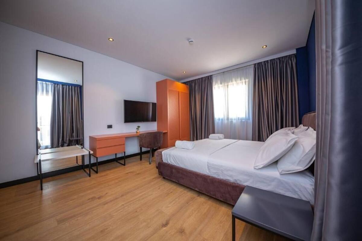 A hotel room with a bed, a desk, a chair, a TV, and a large mirror.