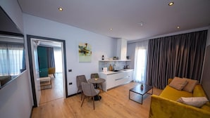 A modern living room with a yellow sofa, a dining area with chairs, a kitchen with a white countertop, and a view through an open doorway. - Apart-Hotel Lili2 (Sarandë)