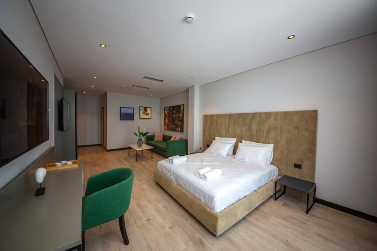 A modern hotel room with a large bed, a green armchair, a small table, and a TV.