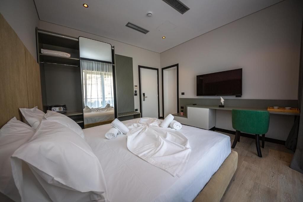 Una camera d'albergo moderna con un letto grande, una scrivania, una sedia, una TV e un armadio.