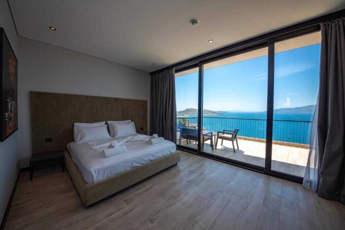 A modern bedroom with a large bed, a view of the sea, and a balcony with outdoor furniture.