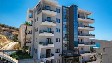 A multi-story hotel with balconies, a central glass elevator, and a view of the sea.