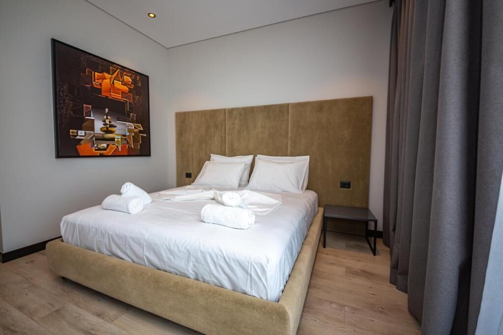 Een moderne hotelkamer met een groot bed, een hoofdbord, een bankje en een schilderij aan de muur.