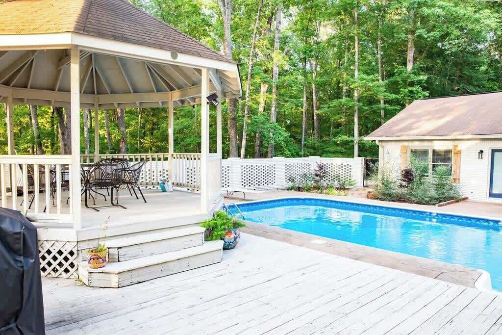 Un espace extérieur abrité comprenant une piscine, une terrasse en bois et un belvédère avec des chaises.
