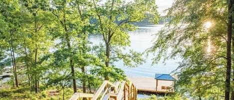 Una terraza de madera que conduce a un muelle sobre un lago, rodeado de abundante vegetación.