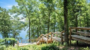 A wooden staircase leading to a bench overlooking a lake surrounded by trees. - Lake T Retreat - Sunset - Pool - Putting Green! (Northport)