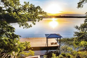 En träbrygga som sträcker sig ut i en stilla sjö, med en solnedgång i bakgrunden.
