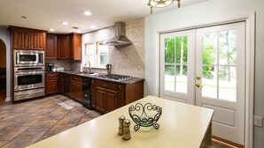 A modern kitchen with dark wooden cabinets, stainless steel appliances, and a large island with a decorative bowl. - Lake T Retreat - Sunset - Pool - Putting Green! (Northport)
