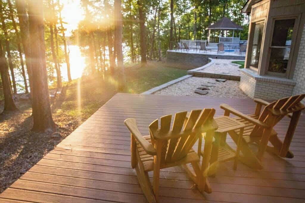 A wooden deck with Adirondack chairs, a gazebo, and a view of a lake.