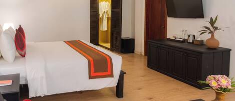 A hotel room with a bed, a desk, a TV, a wardrobe, and a dining table with fruit.