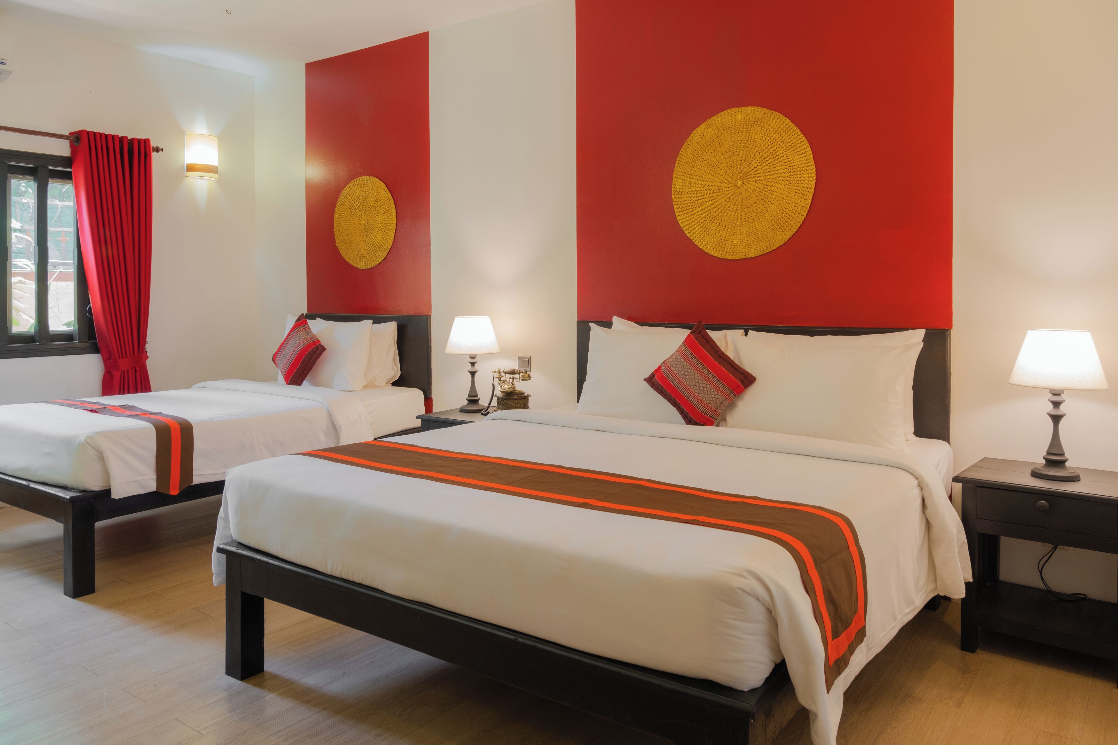 Habitación de hotel con dos camas, cada una con cubrecama blanco y detalles rojos, y una pared grande de color rojo con un diseño circular.