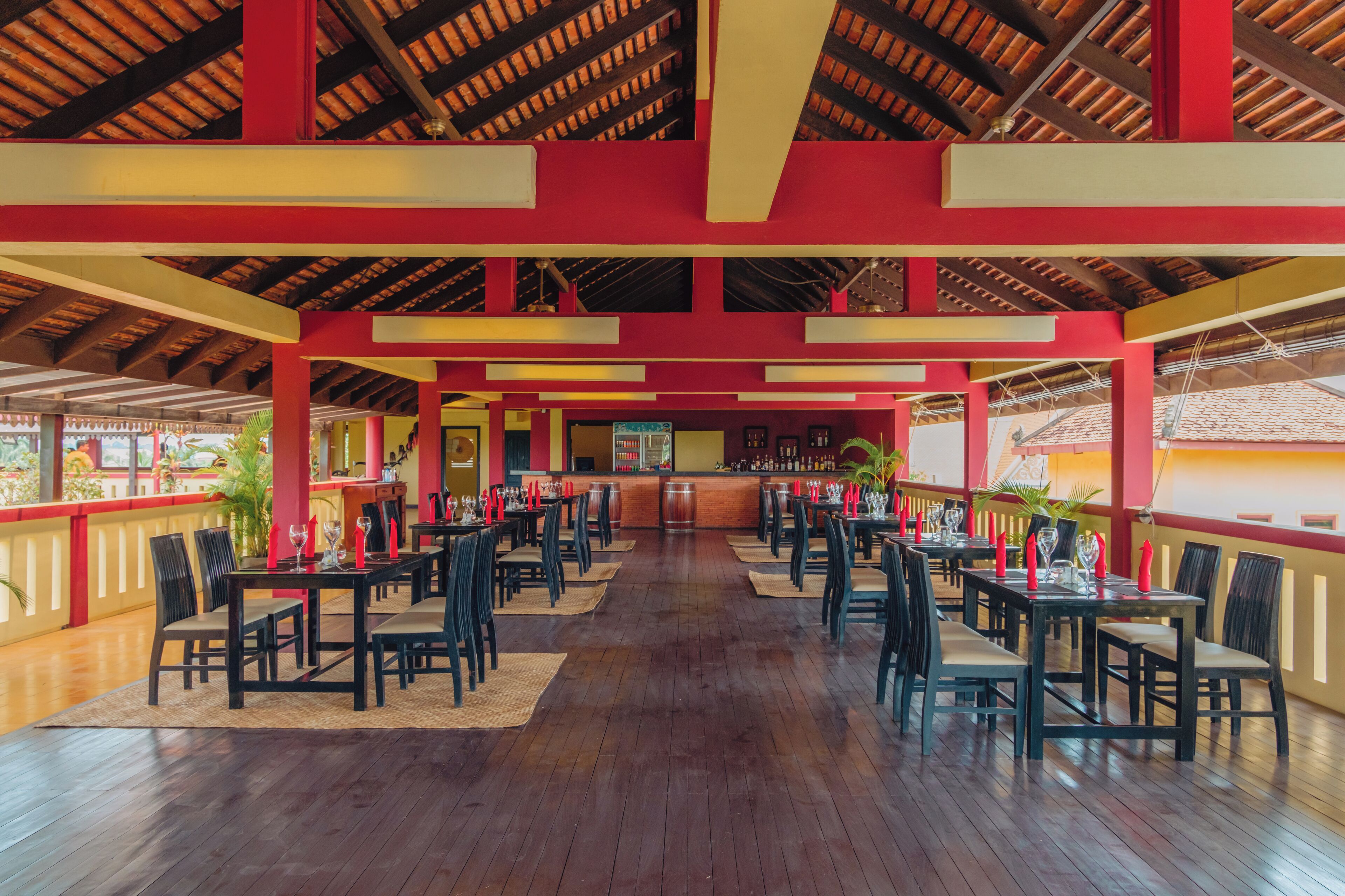 Un restaurante espacioso con pisos de madera y pilares rojos y amarillos. Las mesas están dispuestas con sillas y velas rojas.