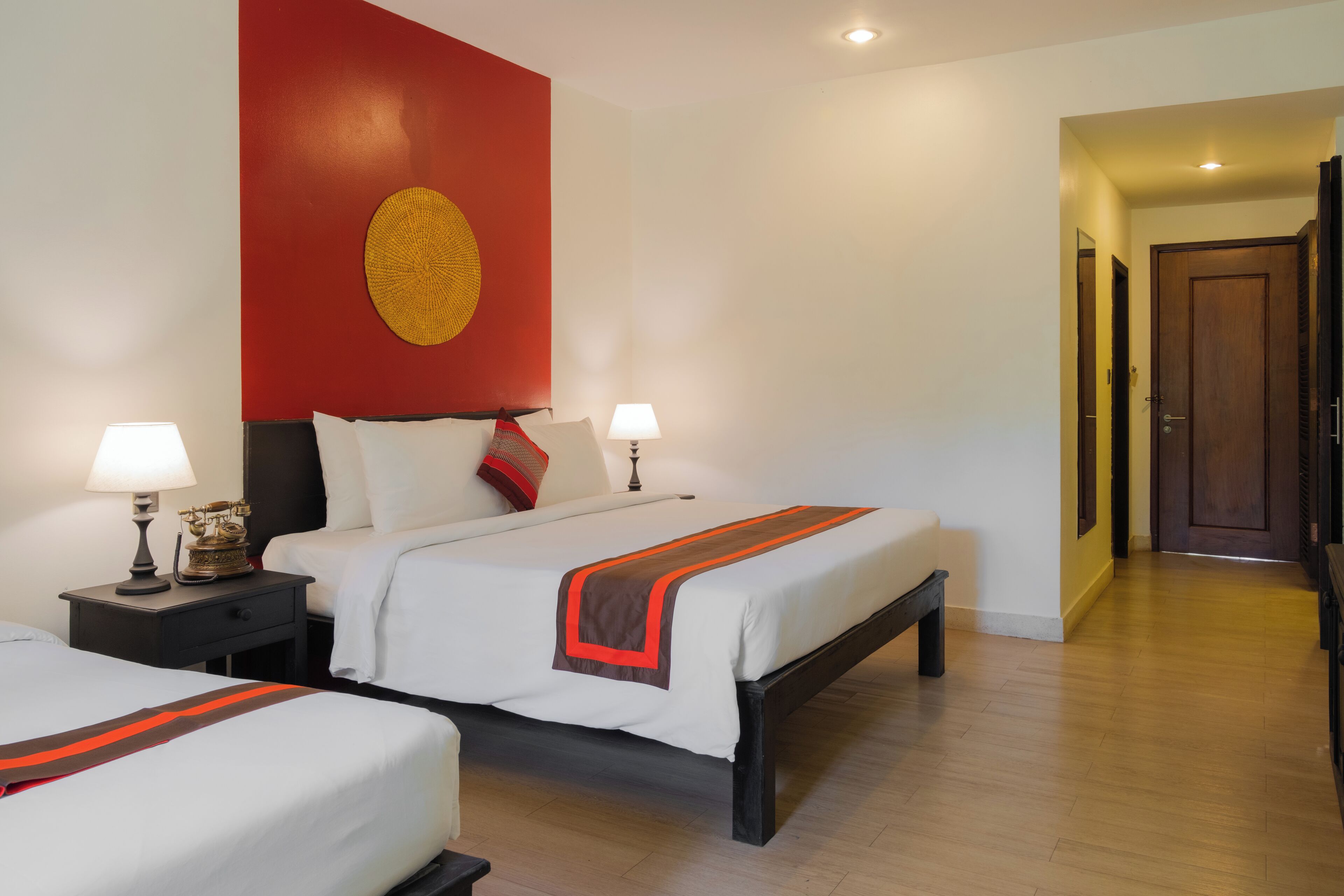 A hotel room with two beds, a red accent wall, and a wooden floor.