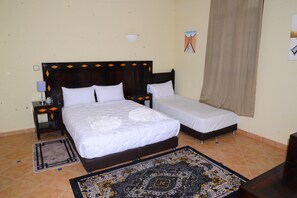 A hotel room with a double bed, a single bed, a nightstand with a lamp, a wall-mounted light fixture, a patterned rug, and a window with a curtain. - Relais d'ourika (Oulad Dlim)