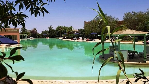 A large, clear swimming pool surrounded by lounge chairs and umbrellas, with a gazebo and palm trees in the background. - Relais d'ourika (Oulad Dlim)