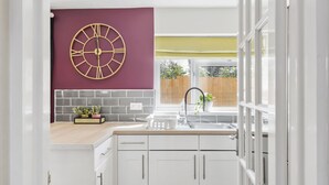 A modern kitchen with white cabinets, a marble backsplash, and a large wall clock. - Luxury House in Bristol with Hot Tub - Sleeps 10 (Bristol)