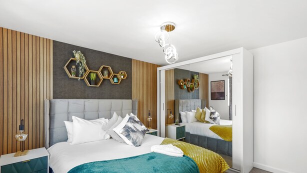 A modern hotel room with a large bed, a mirror, and decorative hexagonal wall panels. - Luxury House in Bristol with Hot Tub - Sleeps 10 (Bristol)