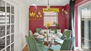 A dining area with a glass table, green chairs, and a red wall with decorative elements. - Luxury House in Bristol with Hot Tub - Sleeps 10 (Bristol)